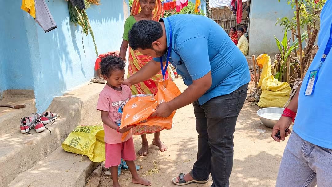 Volunteer giving new clothes to a young child in Simlapal